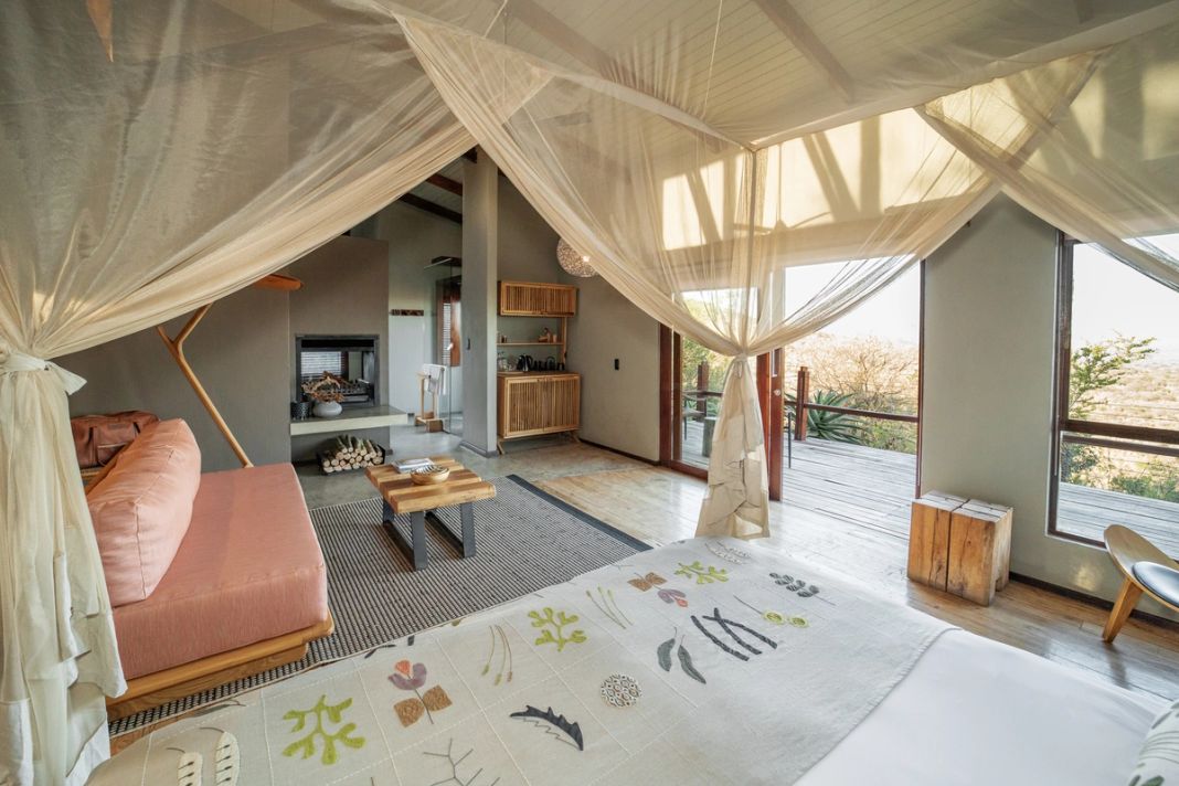 Villa bedroom with a canopy four-poster, a fireplace and kitchenette at left and a pink loveseat.
