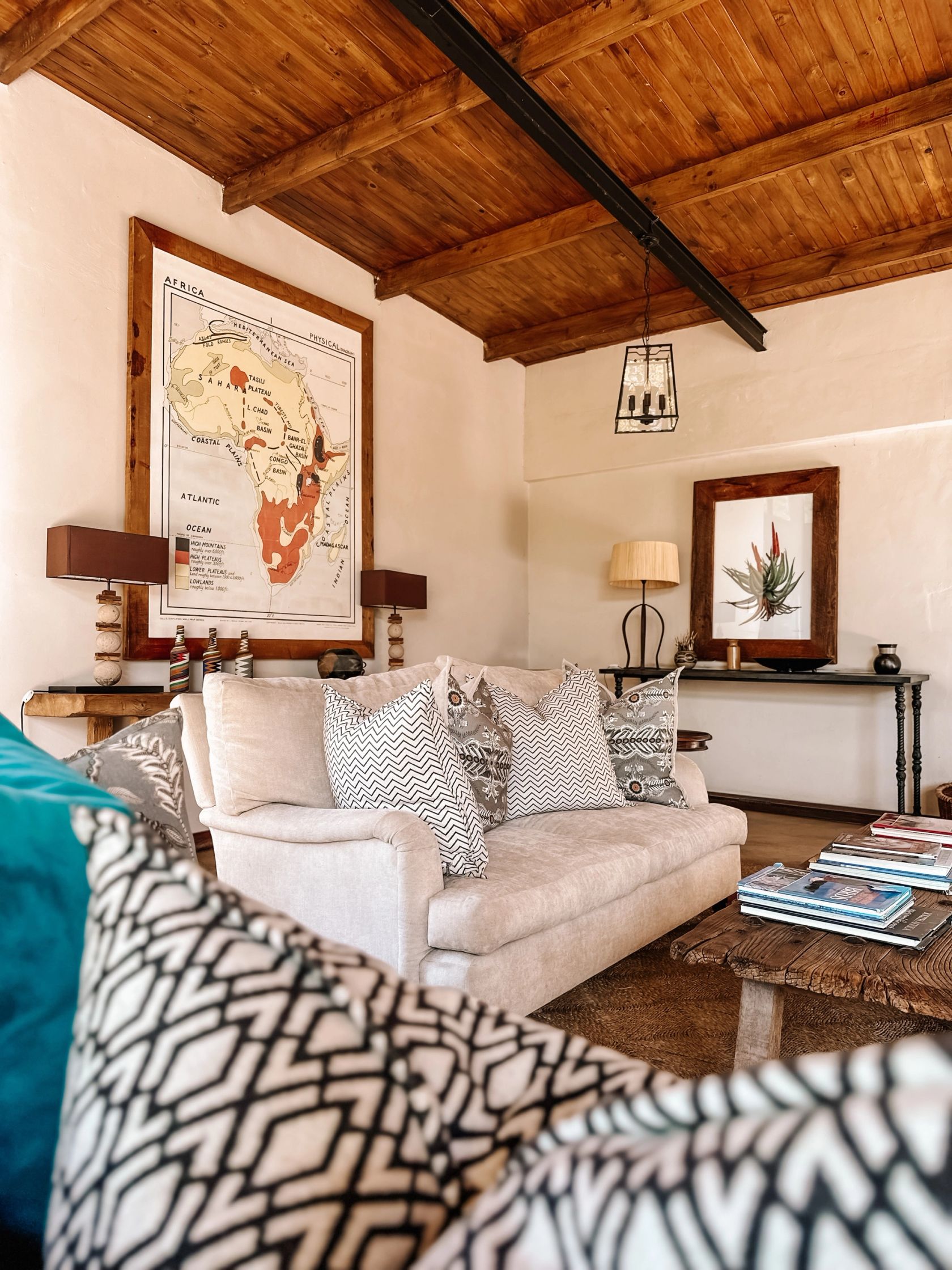 A lounge with a framed physical map of Africa, a cream sofa, and a timber-beamed ceiling.