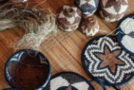 Woven palm baskets, lidded pots and coasters rest on a bamboo mat with loose weaving grass.