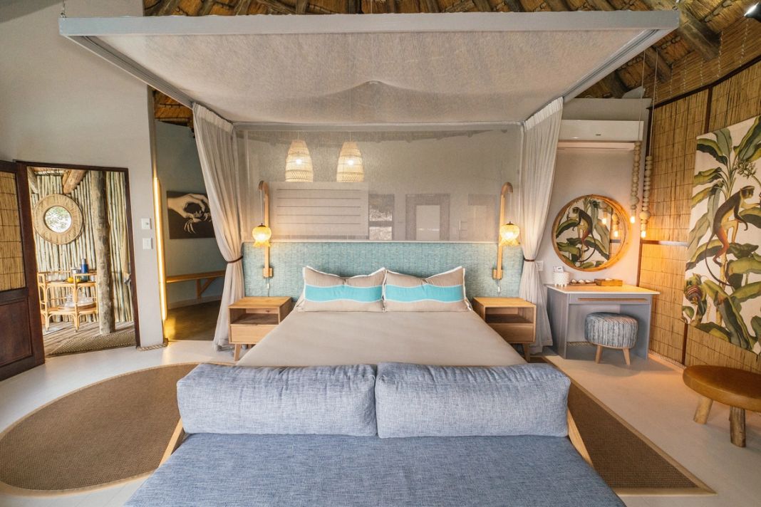 A king four-poster with a turquoise-tile headboard, a blue daybed and a dressing table with a round mirror.