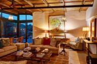A lounge with sofas, a book-stacked coffee table, and a framed physical map of Africa on the wall, lit by lamps at dusk.