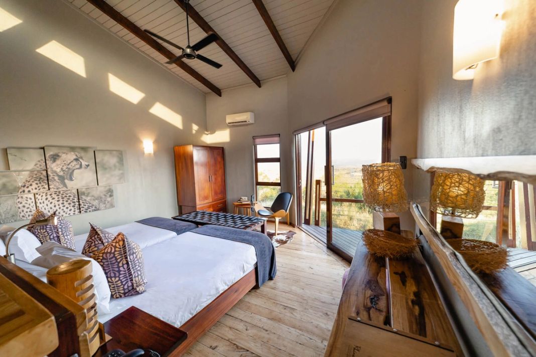 A safari room with framed cheetah art, a ceiling fan, a plain headboard and glass doors to a bush-view deck.