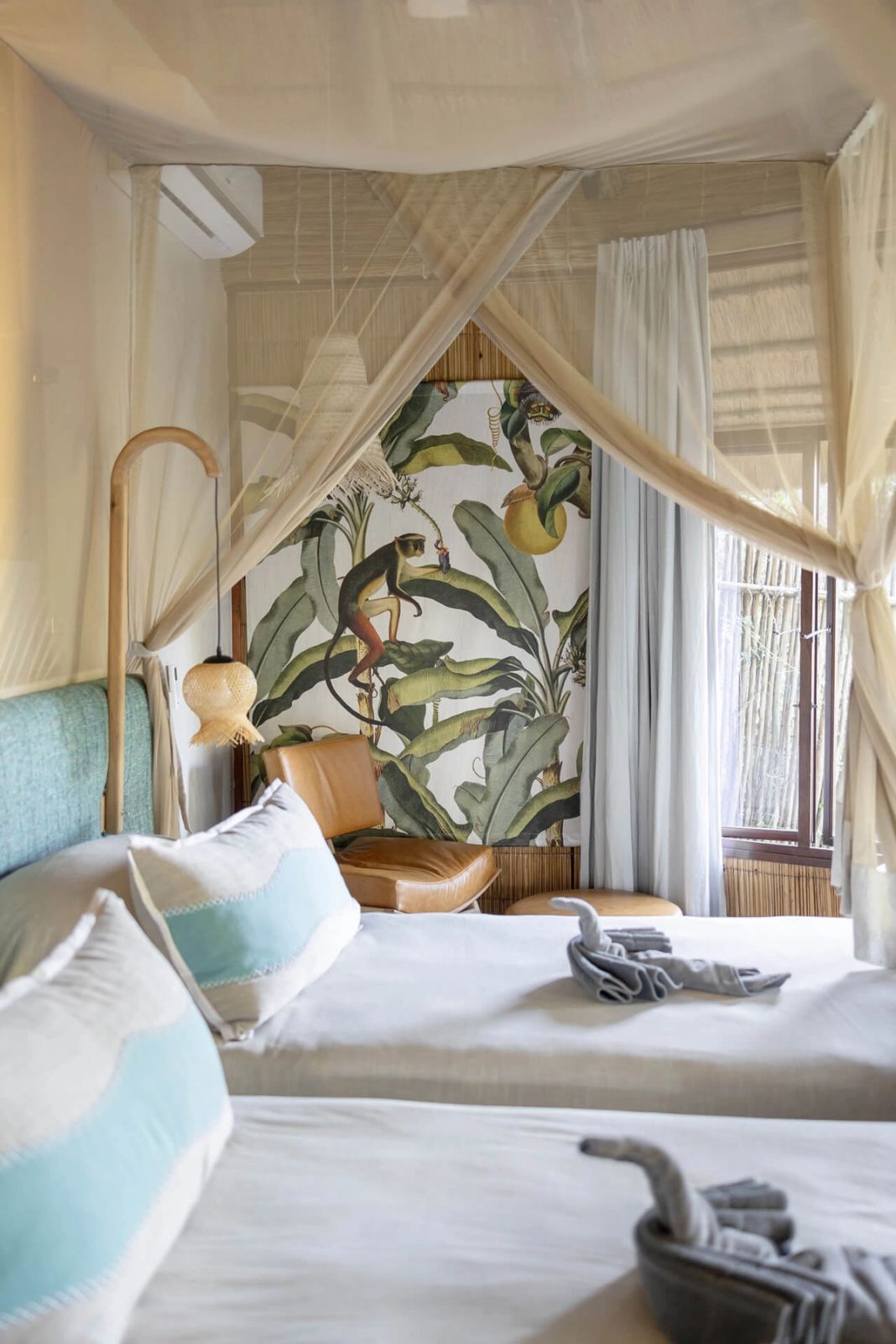 Two single beds side by side under mosquito nets, with folded-towel animals and a banana-leaf wall print.