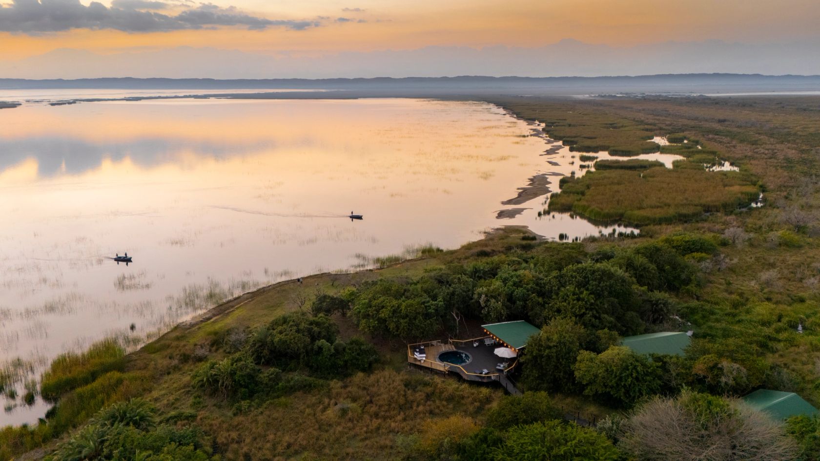 Dawn over Lake St Lucia, local fishing boats crossing the pink water below the lodge pool deck.