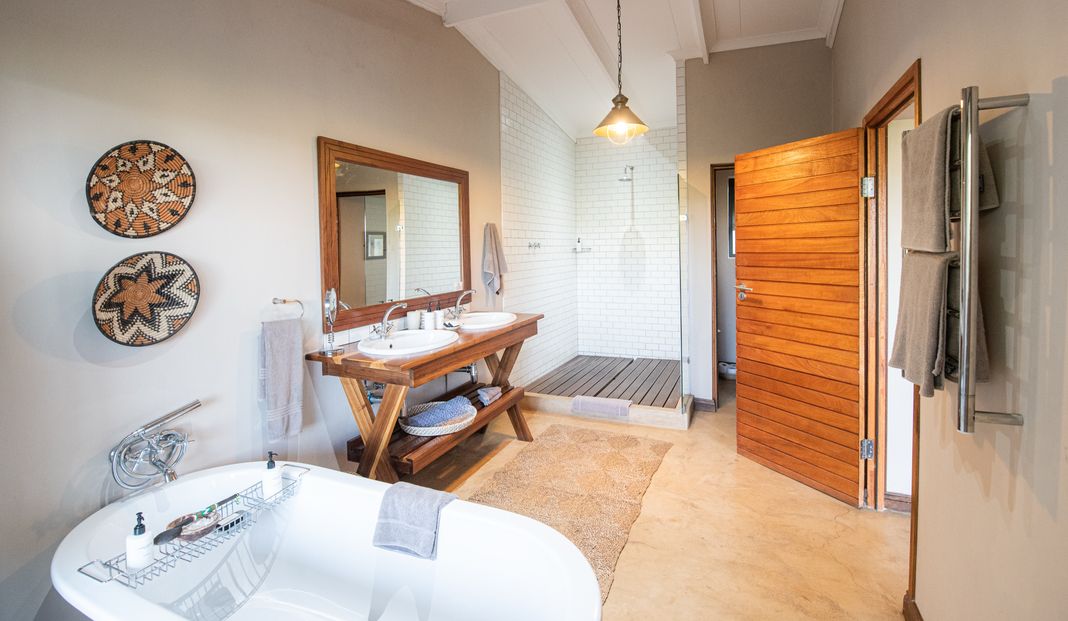 A lodge bathroom with a freestanding tub, twin basins on a wooden vanity and a tiled walk-in shower.