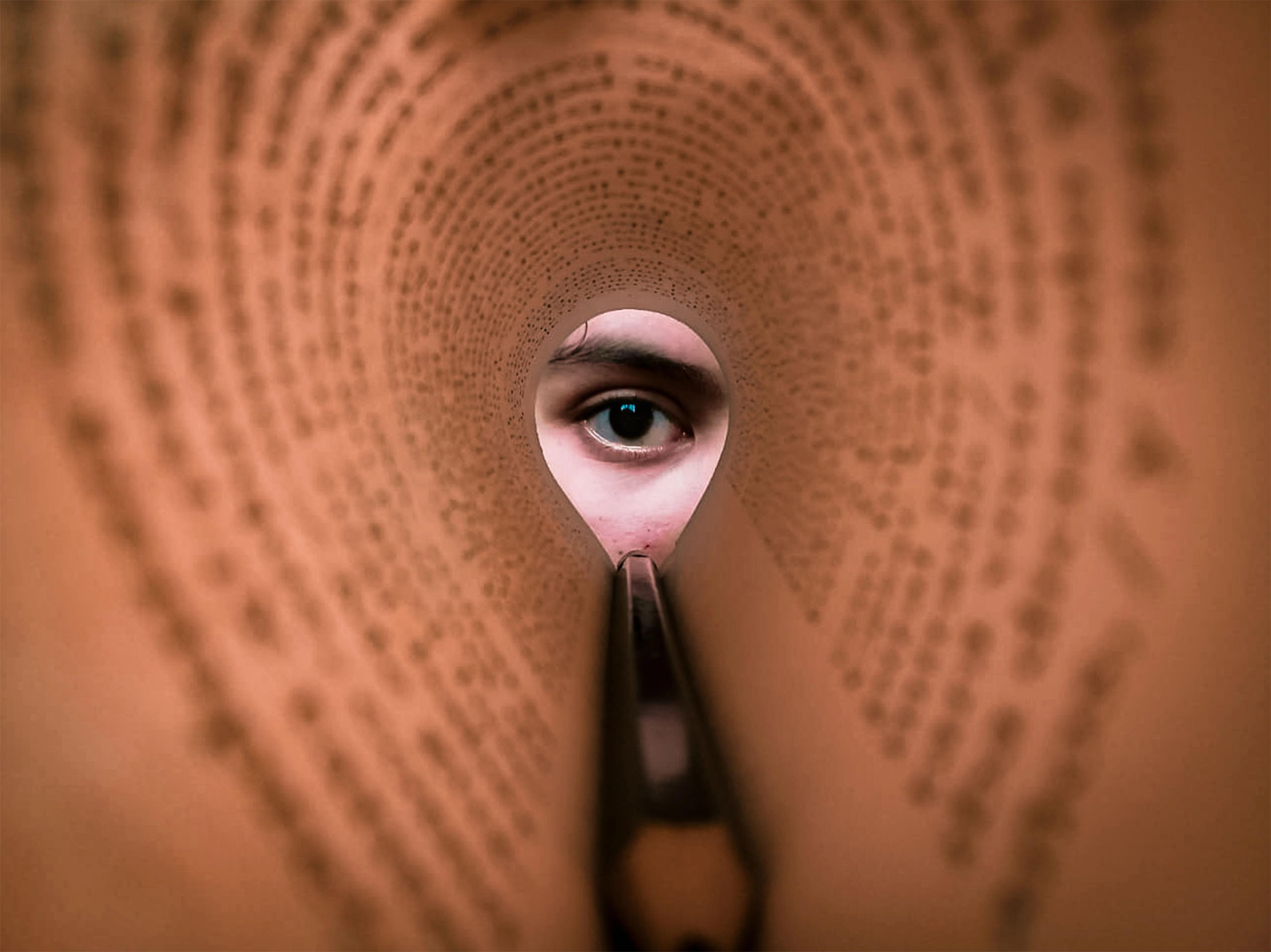 An eye looking through a rolled up newspaper