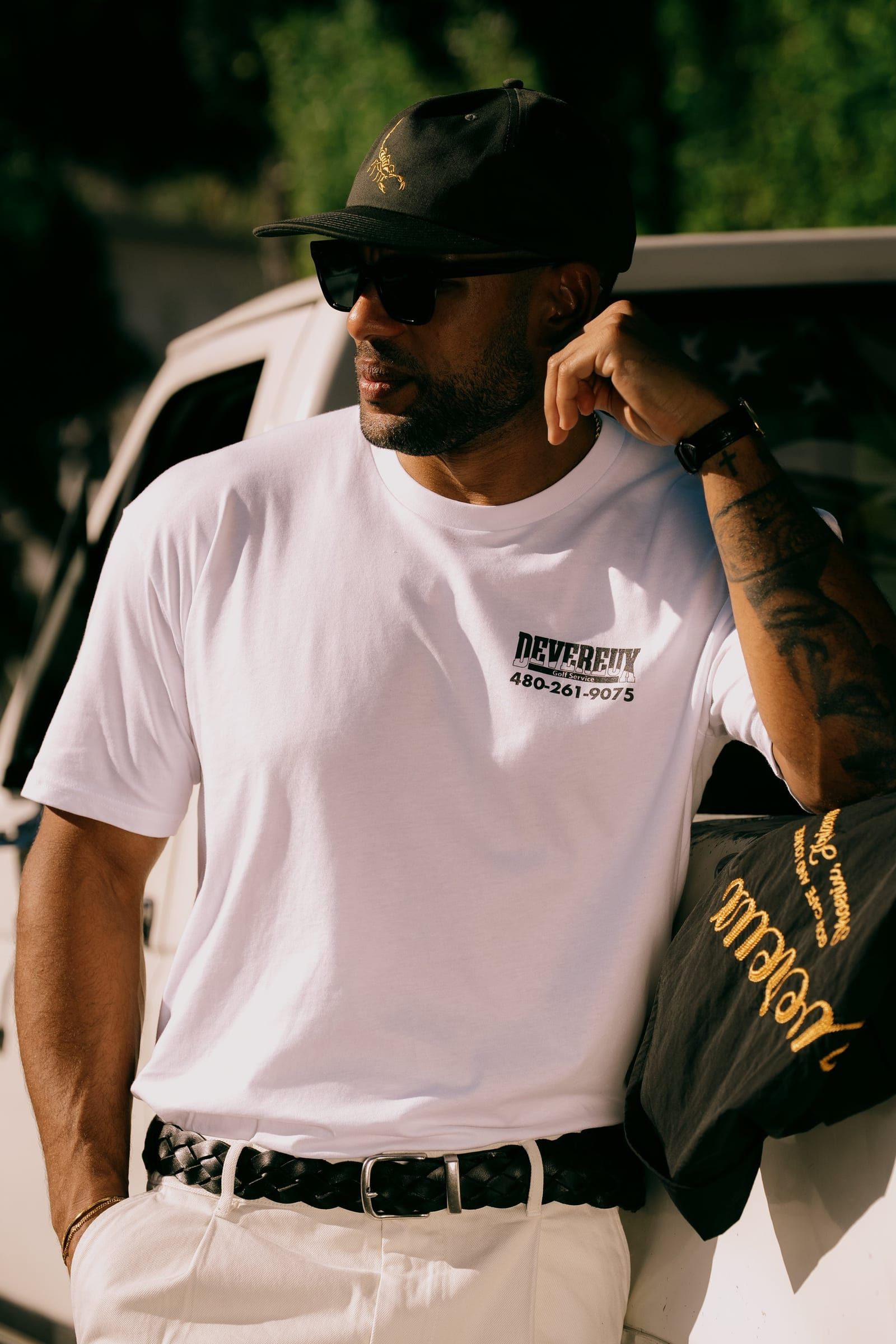 Devereux campaign: model in a white logo tee and black scorpion cap leaning against a vintage truck