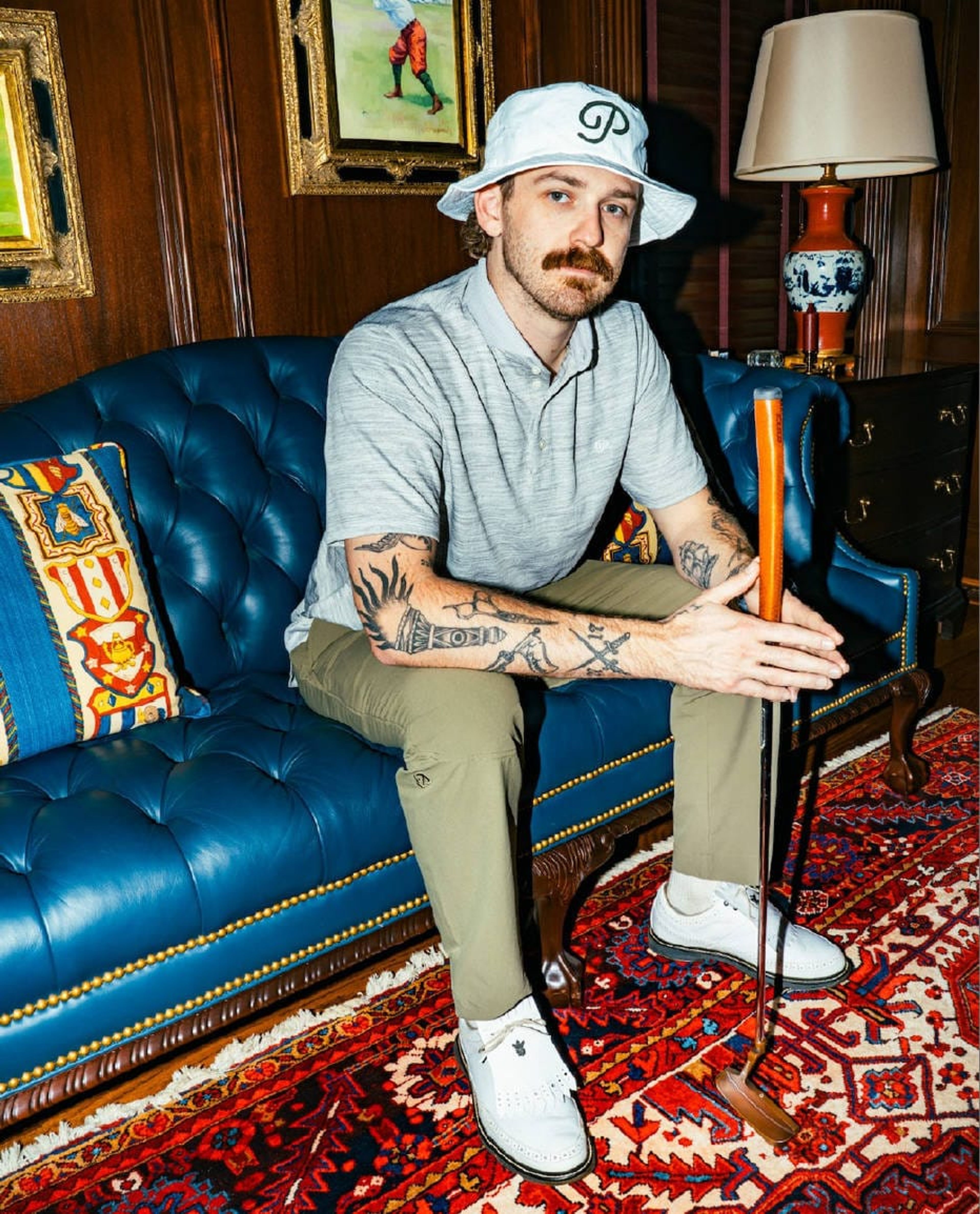 Public Drip campaign: golfer in a bucket hat and heather polo seated on a leather Chesterfield, holding a putter