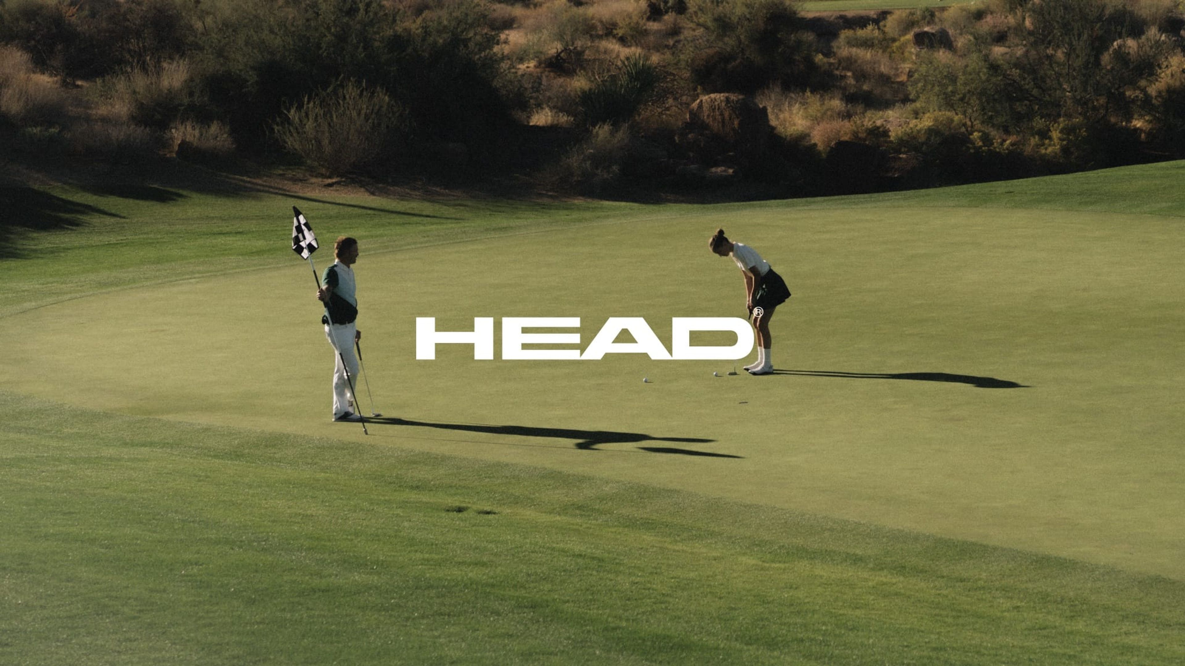 HEAD wordmark over a desert golf course, two players on the green