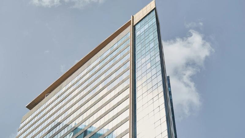 A modern glass-walled commercial office building against a clear blue sky.