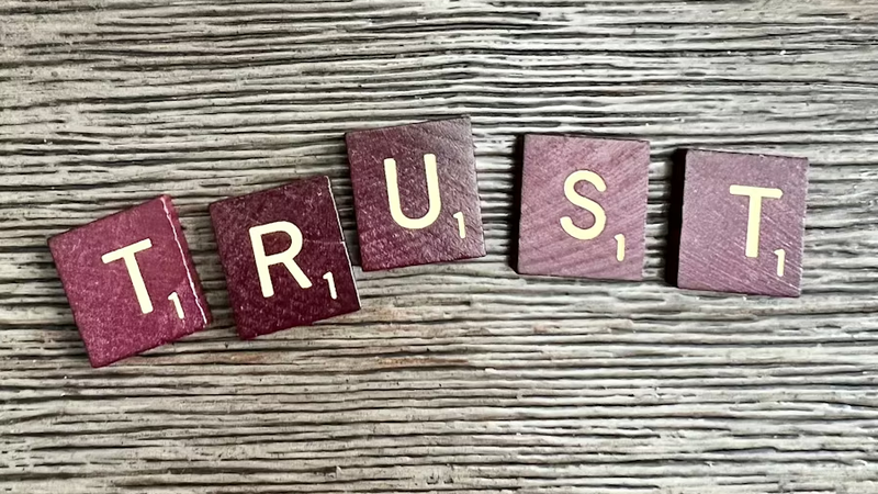 Wooden letter blocks spelling TRUST — representing the governance frameworks, escalation rules, audit trails, and human-in-the-loop controls that AI agents in facilities management need to earn operational trust in safety-critical environments.