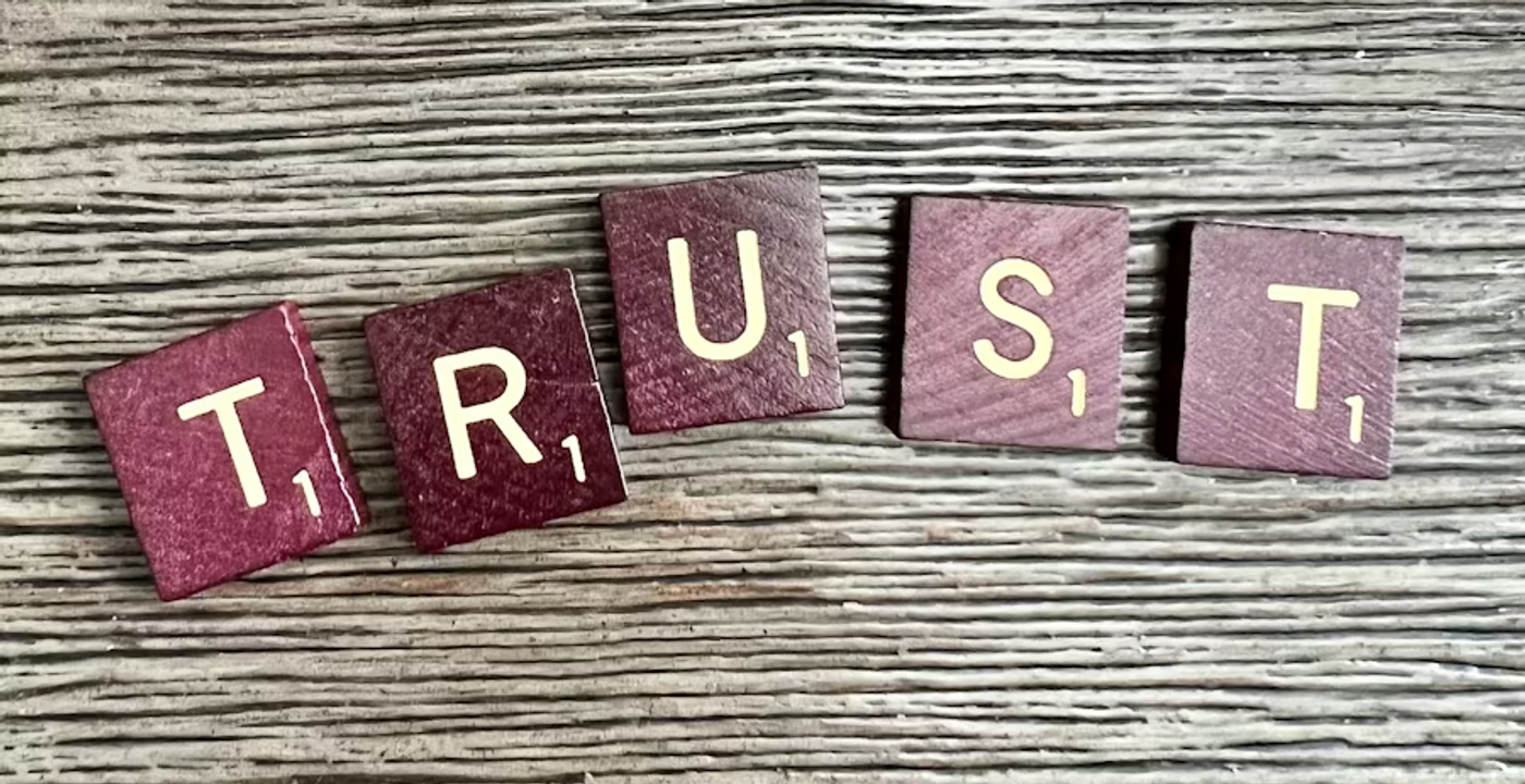 Wooden letter blocks spelling TRUST — representing the governance frameworks, escalation rules, audit trails, and human-in-the-loop controls that AI agents in facilities management need to earn operational trust in safety-critical environments.