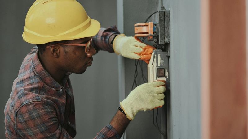 A construction worker in a yellow hard hat and safety goggles stands at a building site.
