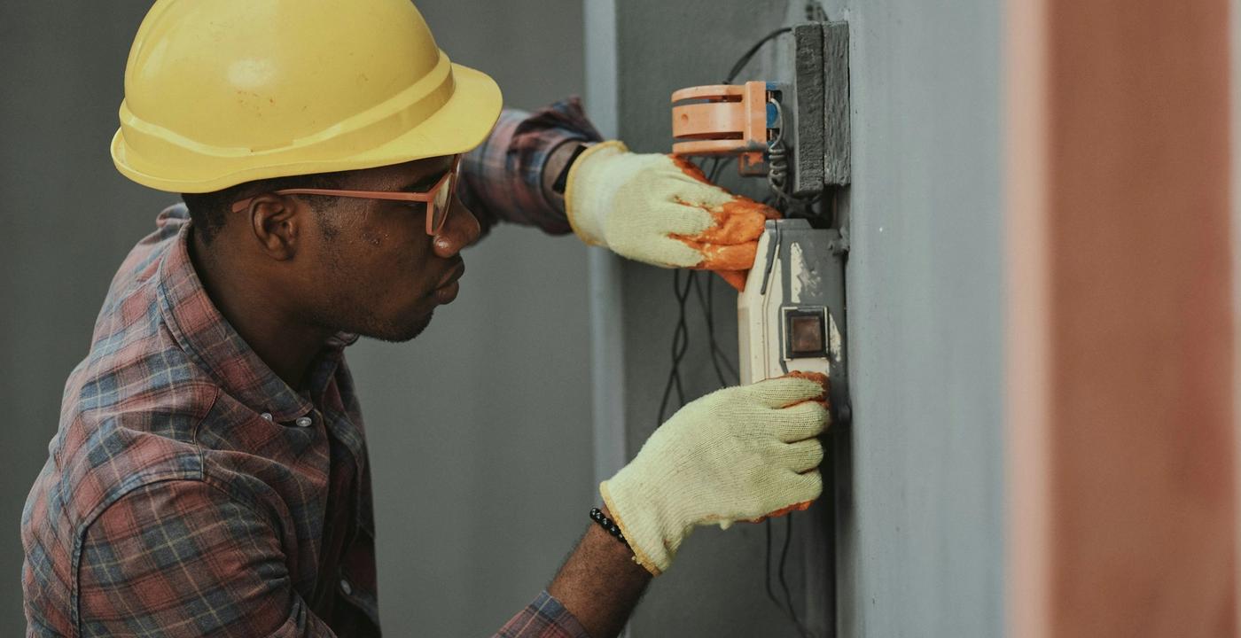 A construction worker in a yellow hard hat and safety goggles stands at a building site.