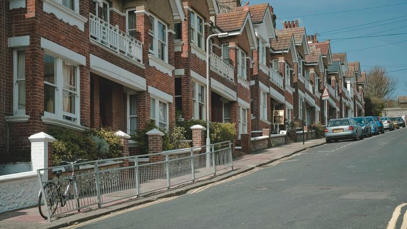 A residential street in Brighton, UK: a row of brick and rendered houses beside the road in daytime.