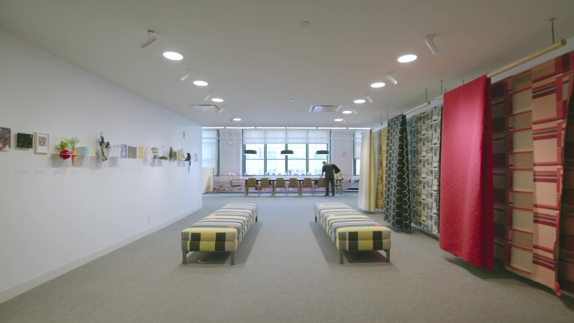 Designtex showroom with patterned textile panels hanging along the wall and upholstered benches on the floor