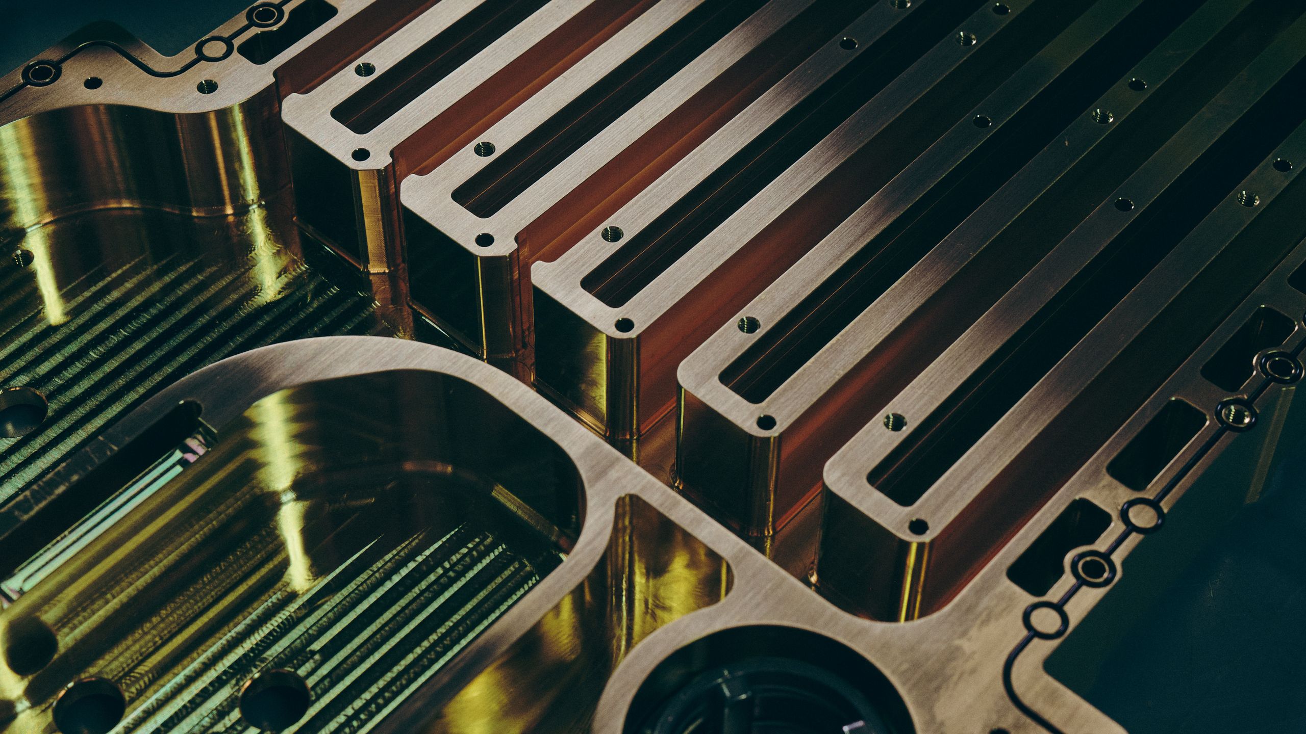 Machined copper busbars laid into a polished steel fixture, catching warm gold reflections