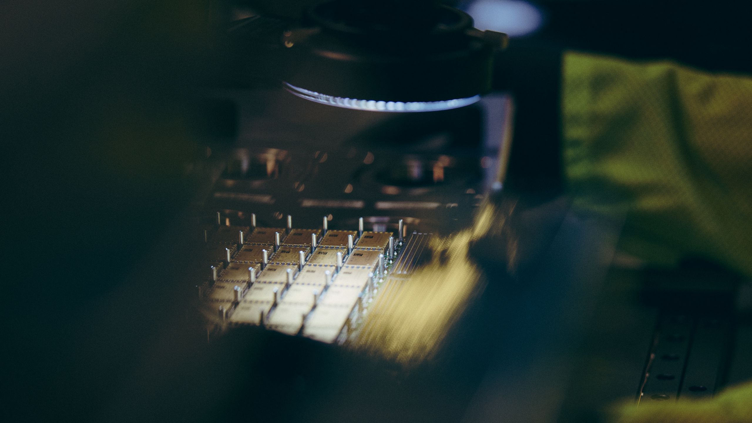 Close-up of a gloved hand working over a row of components under a bright ring light