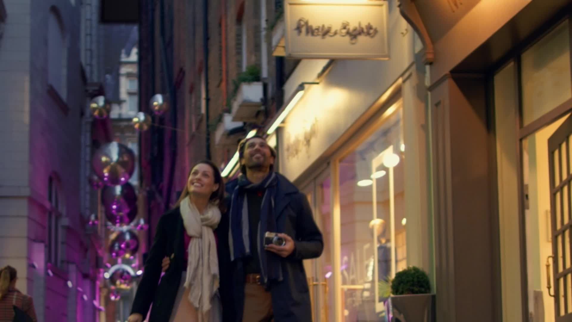 A couple walking a festively lit shopping street at dusk