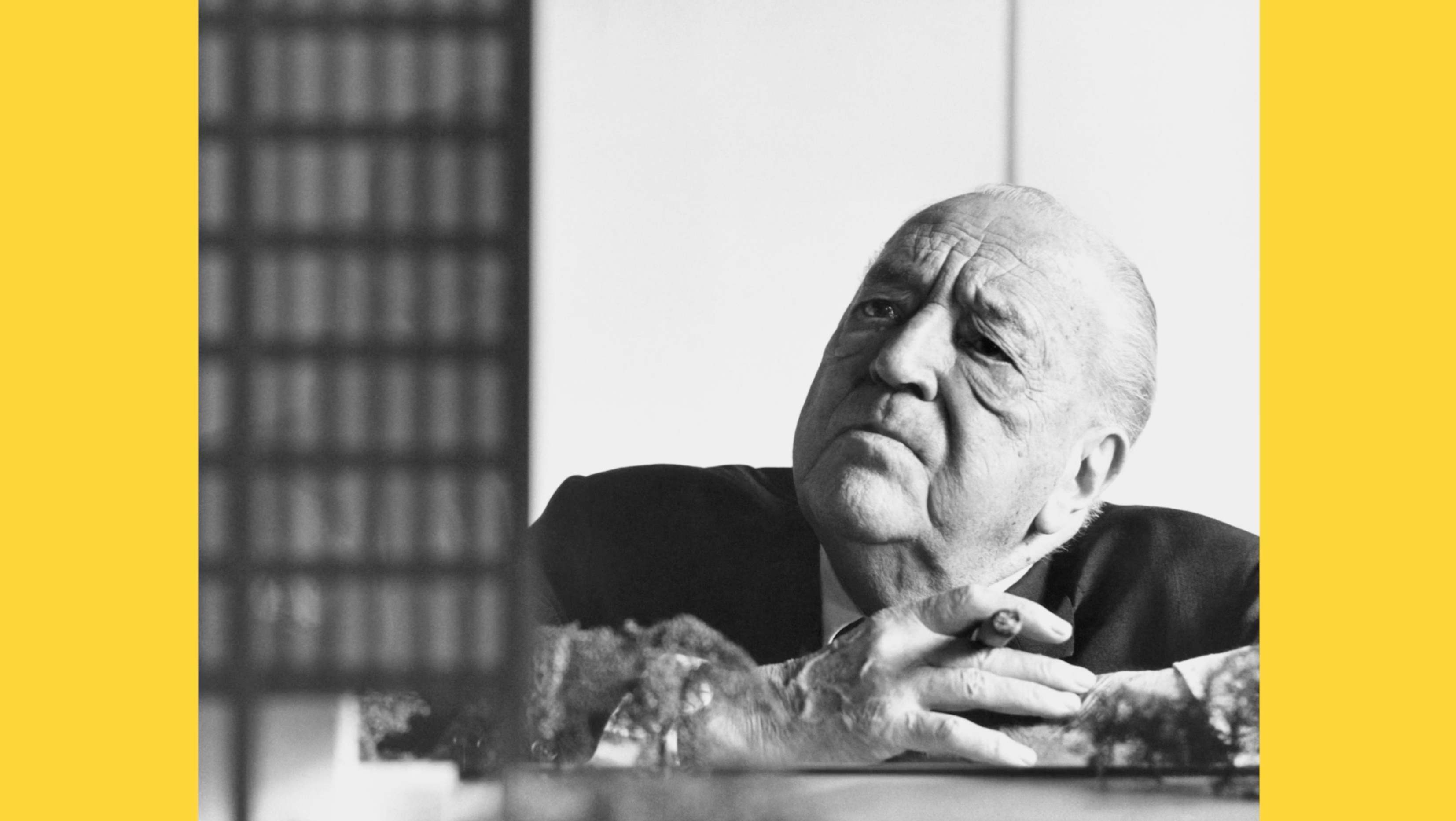Black and white archival film still of a modernist architect studying a building model