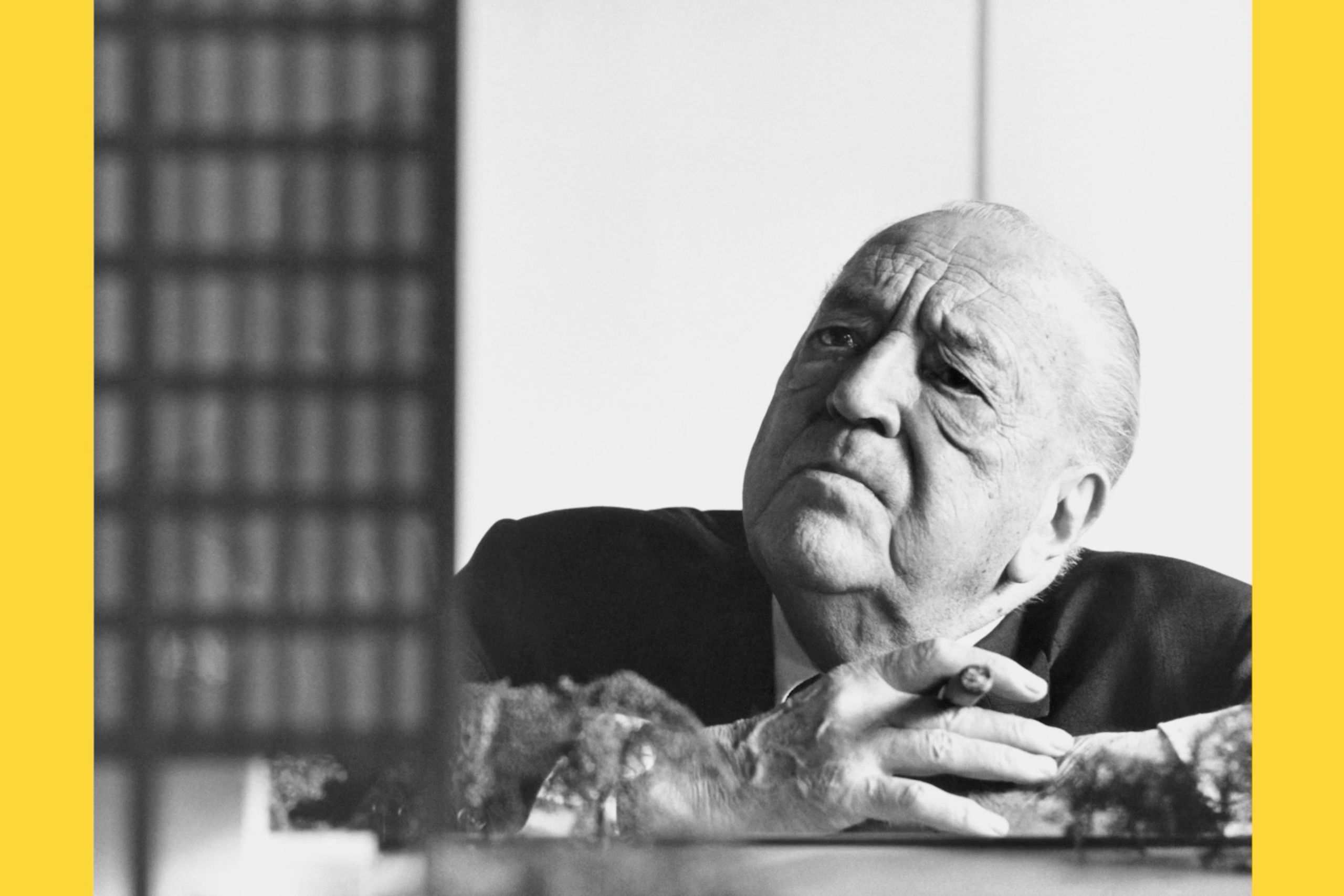 Black and white archival film still of a modernist architect studying a building model