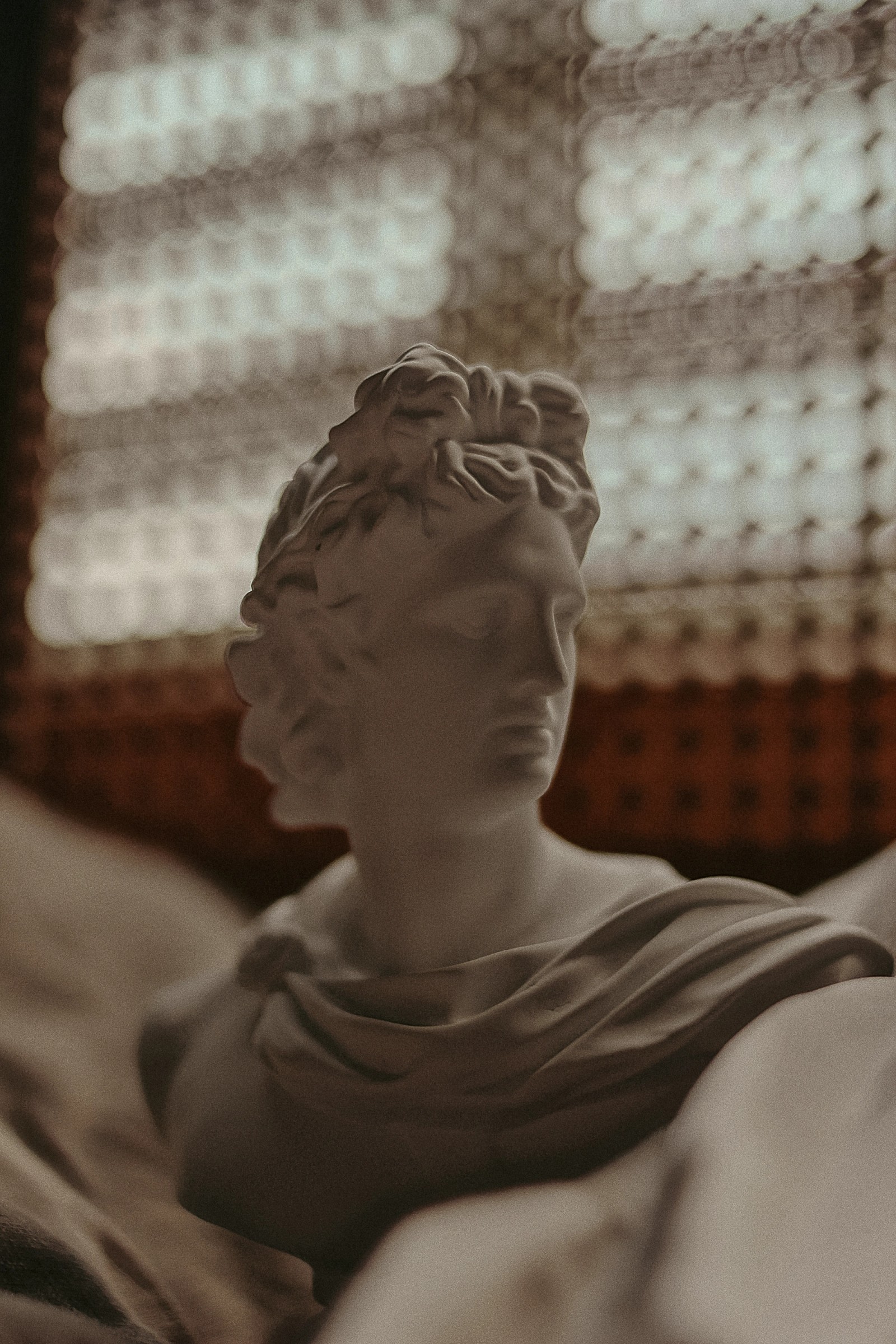 White bust of Apollo against a blurred background with patterned light bokeh.