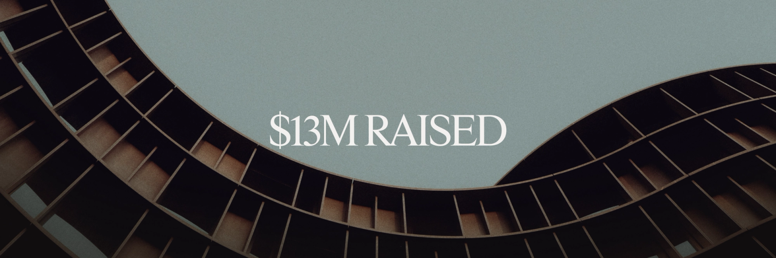 Text "$13M RAISED" above a modern building with curved, slatted wooden architecture against a grey sky.