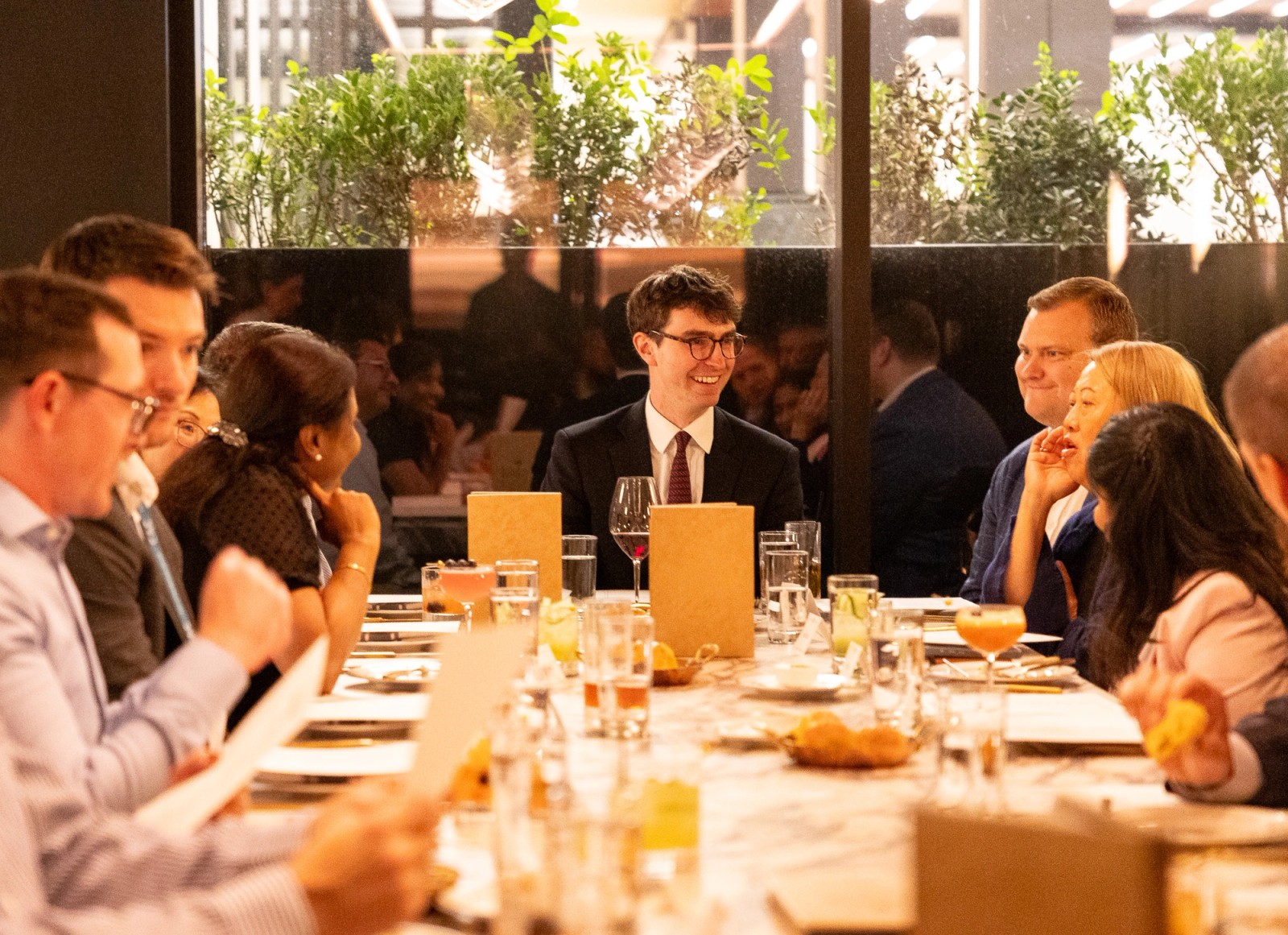 A diverse group of professionals smiling and conversing at a restaurant table.