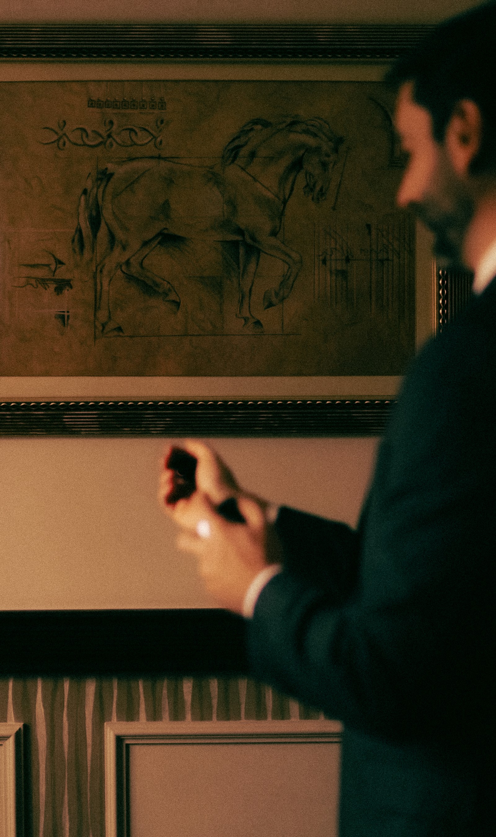 A man in a suit adjusts his cuff in front of a framed drawing of a horse.