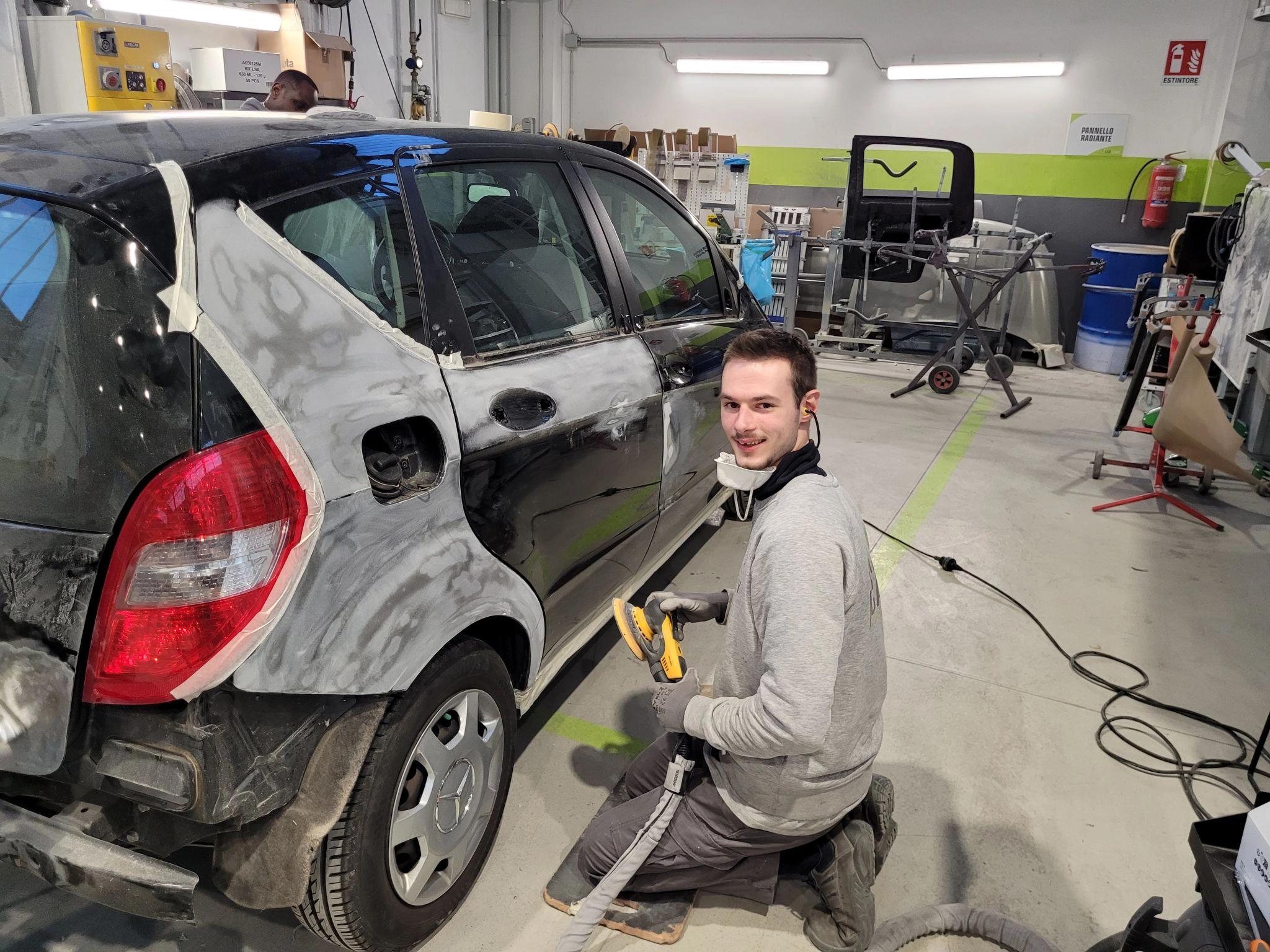 Ragazzo lavora alla riparazione della carrozzeria di una macchina