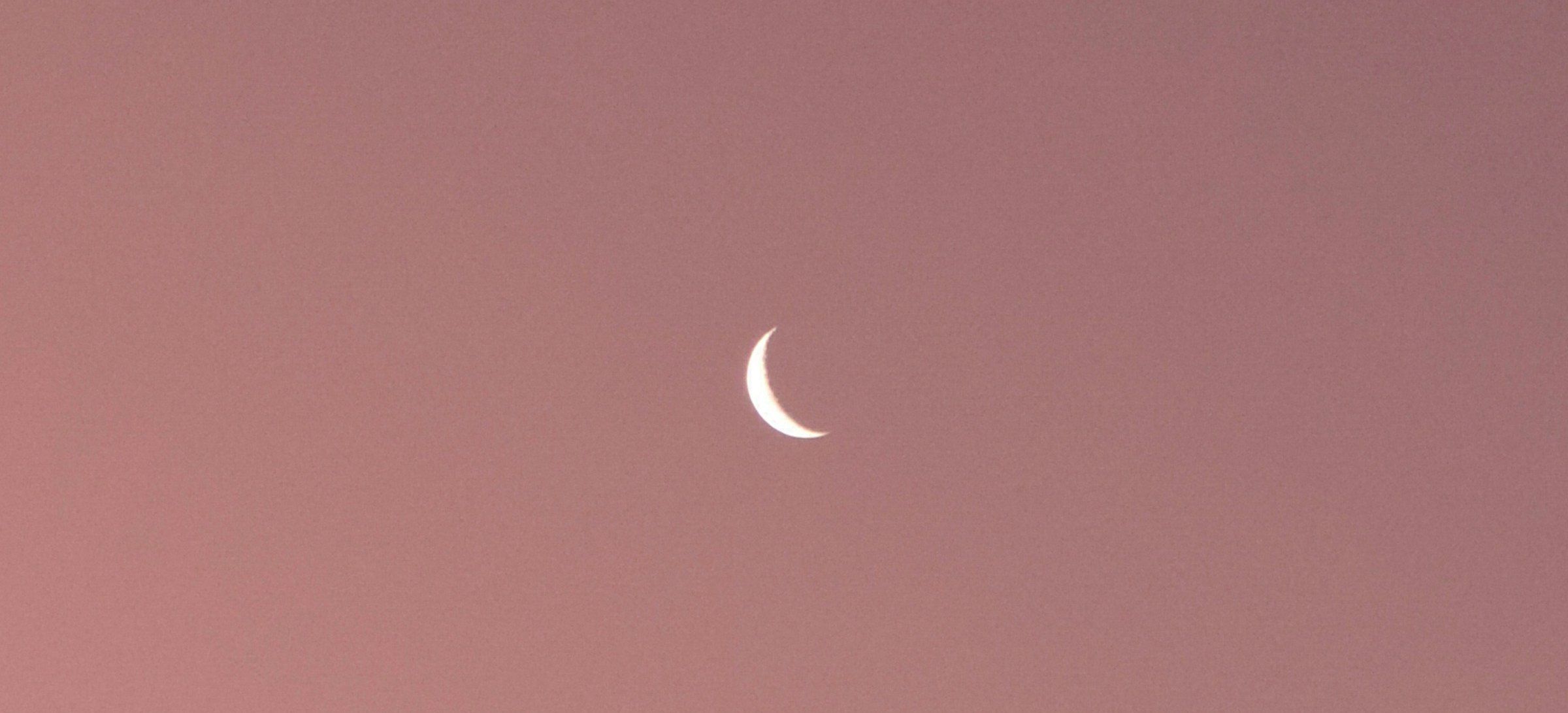 Een smalle maansikkel in een roze avondlucht