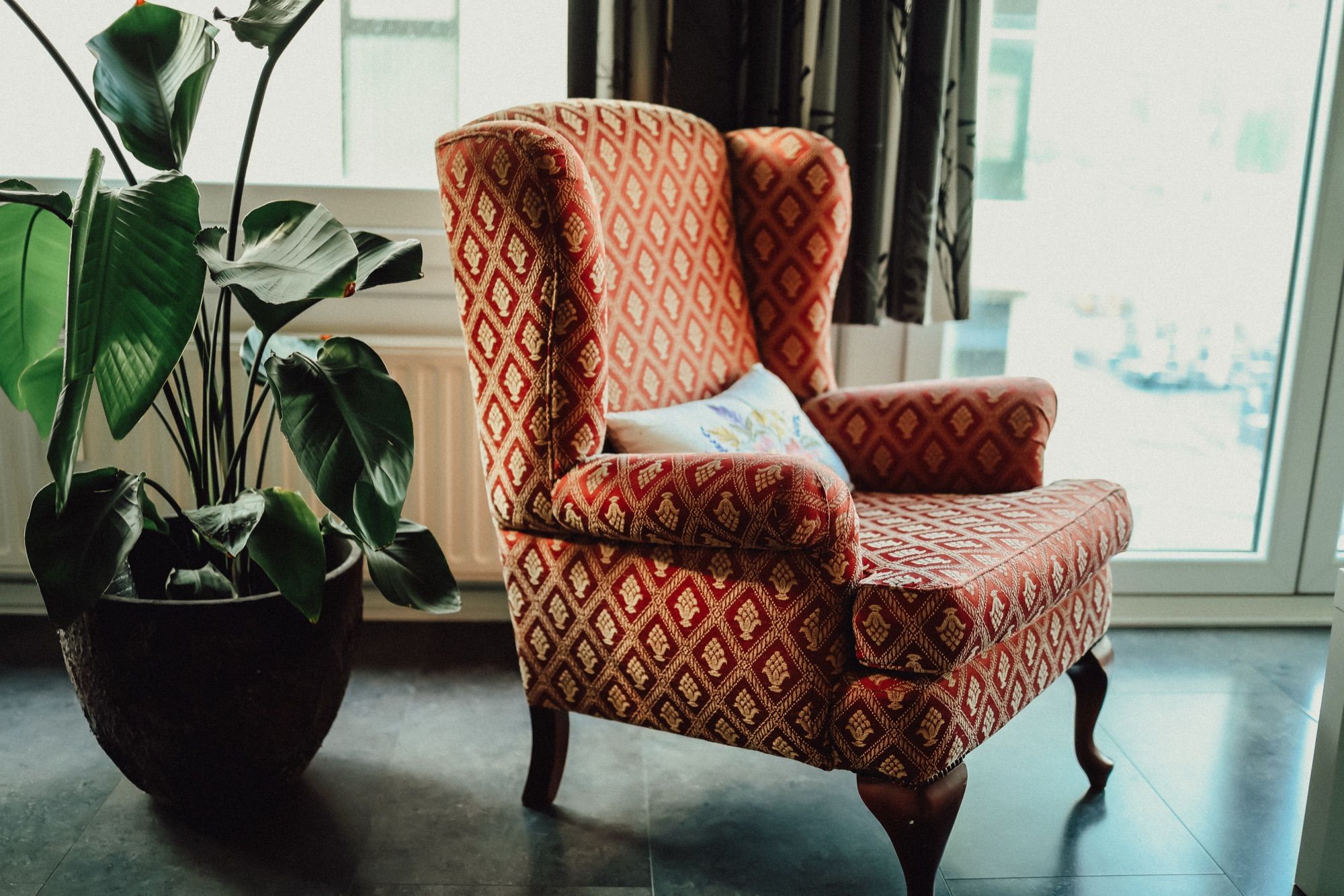 Een oranje fauteuil bij het raam, tussen de kamerplanten