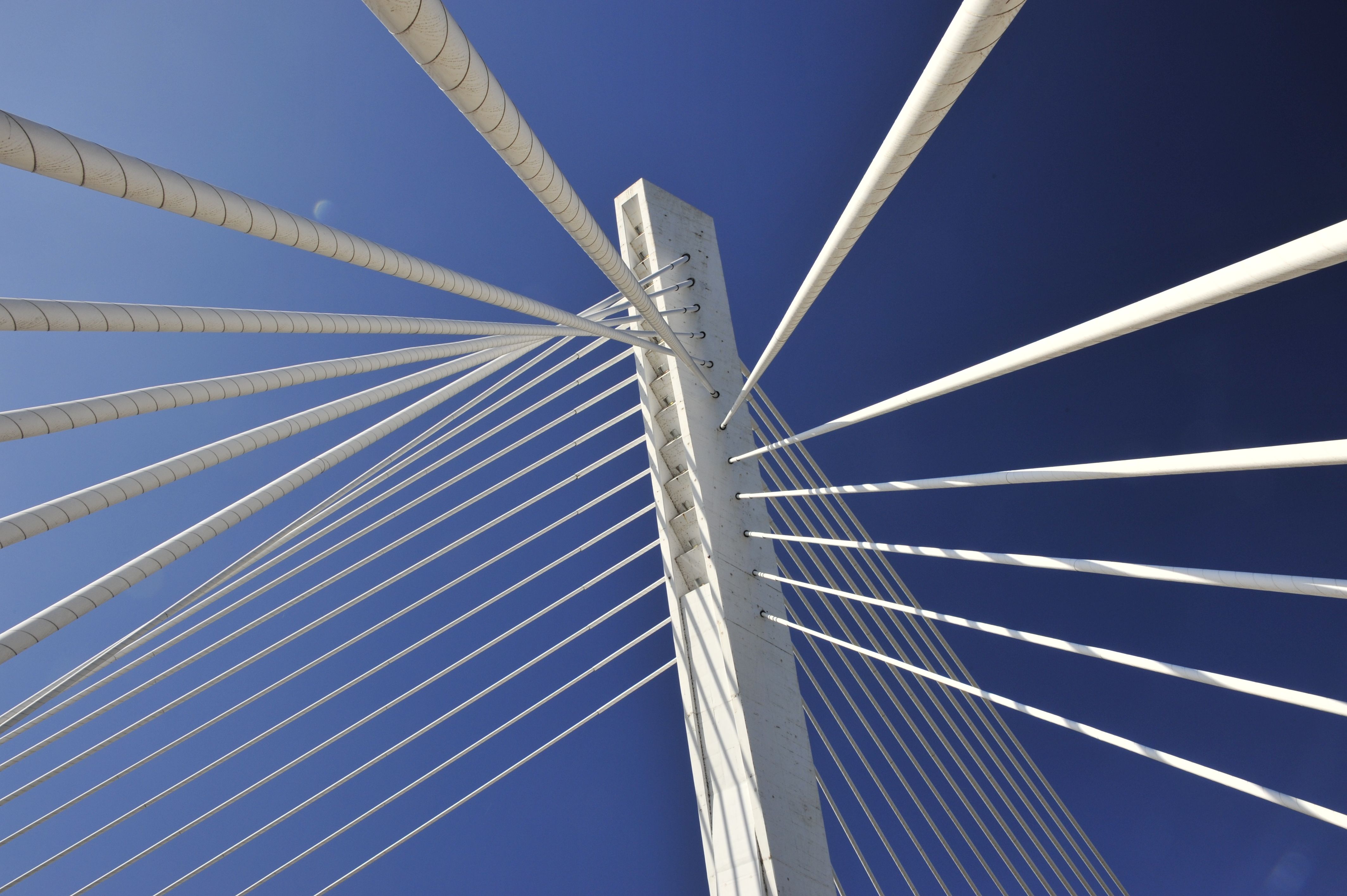Un détail architectural à contre-plongée du pylône blanc et des câbles du pont du Millénaire sur fond de ciel bleu clair.