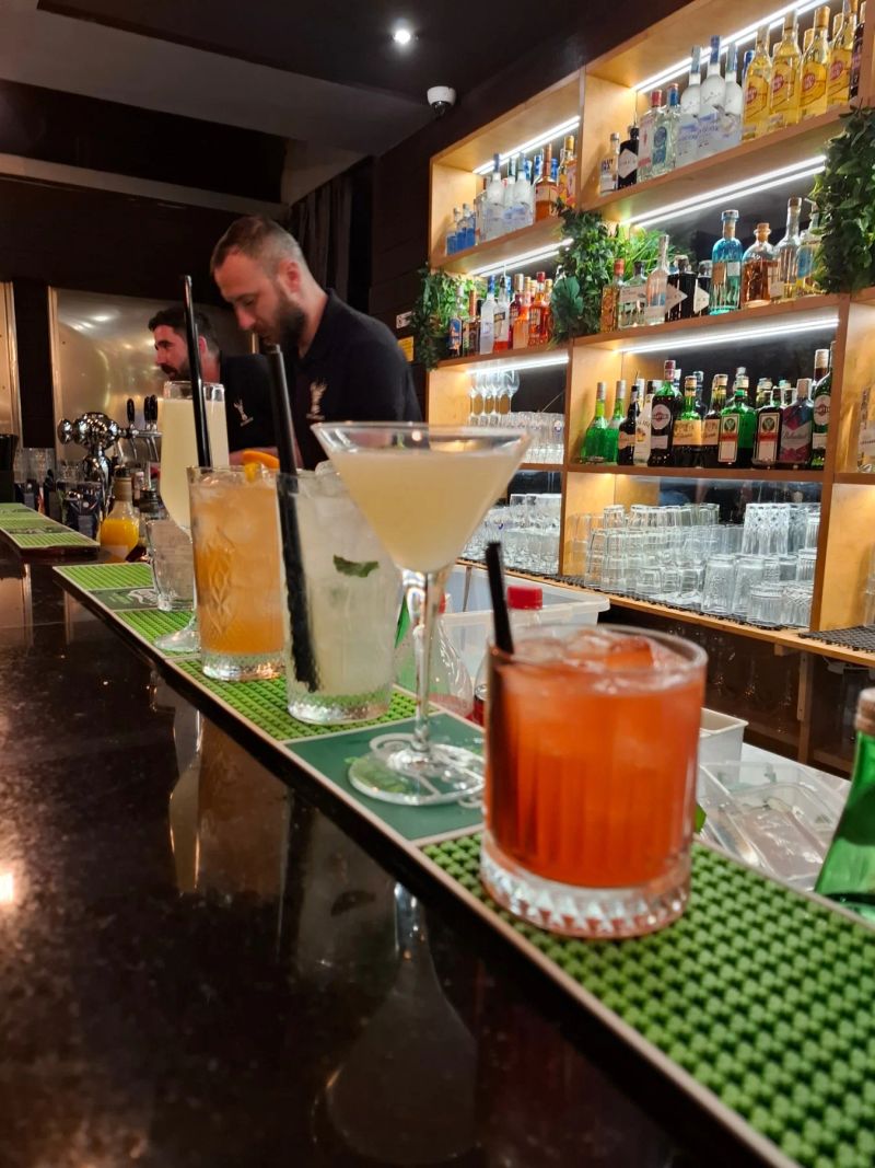 A row of expertly crafted cocktails, including a martini and a mojito, lined up on a modern bar counter.