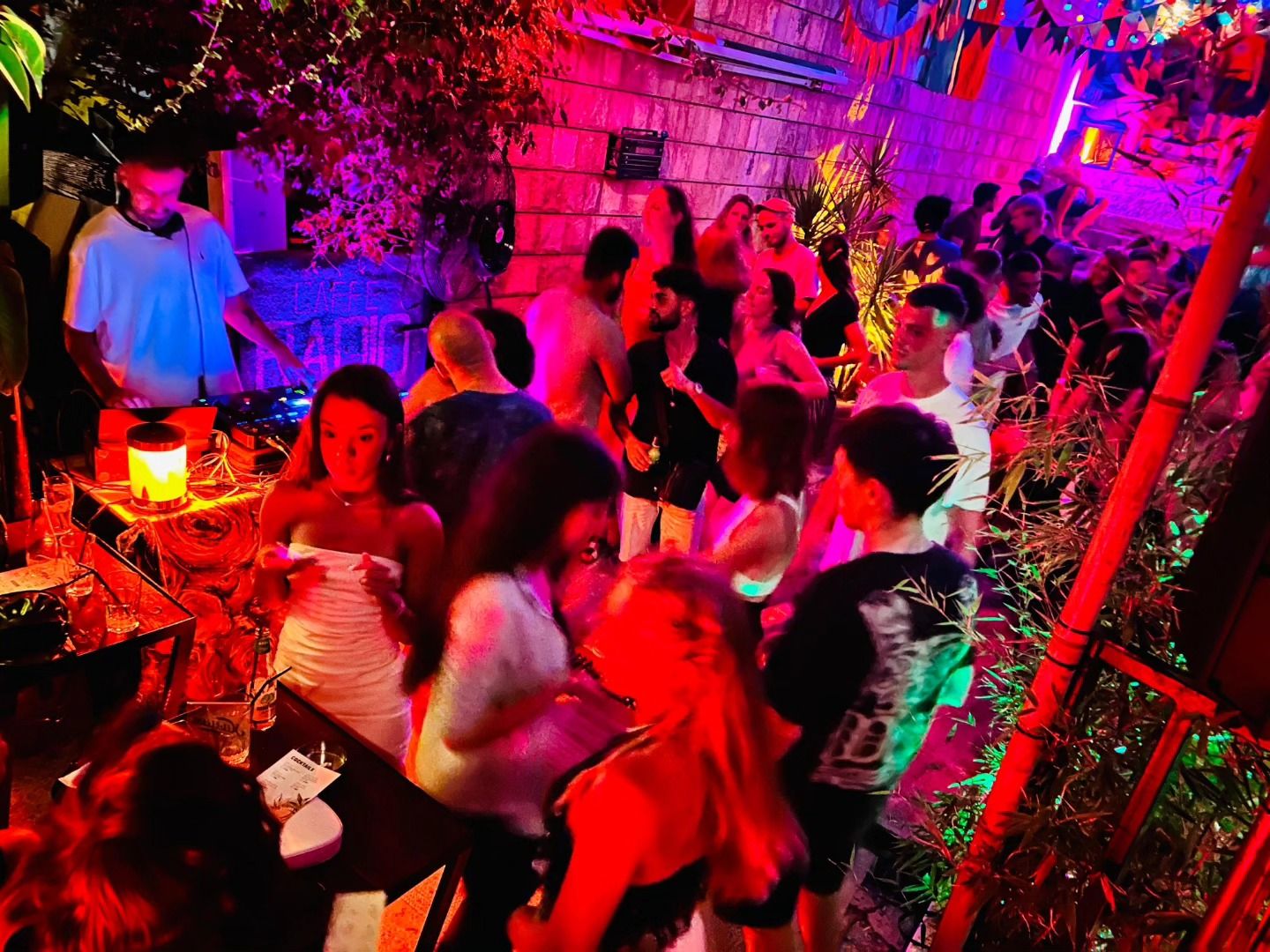 An energetic night party with people dancing close to the DJ booth, illuminated by red and green lights.
