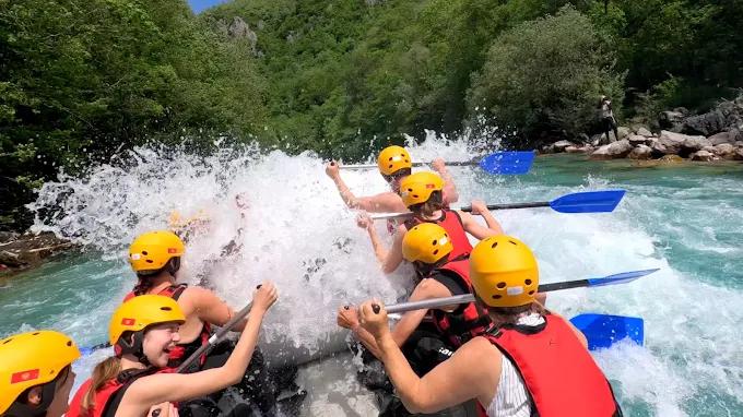 A view from inside the raft, showing a team of adventurers paddling hard as they crash through a large wave.
