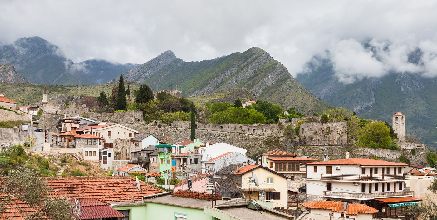 A panoramic view of the fortified old town of Stari Bar, nestled on a hillside with dramatic mountains in the background.