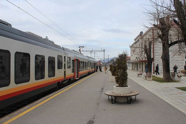 列客运火车停在黑山尼克希奇火车站的站台上，车站大楼在右侧，人们在阴天下的站台上活动