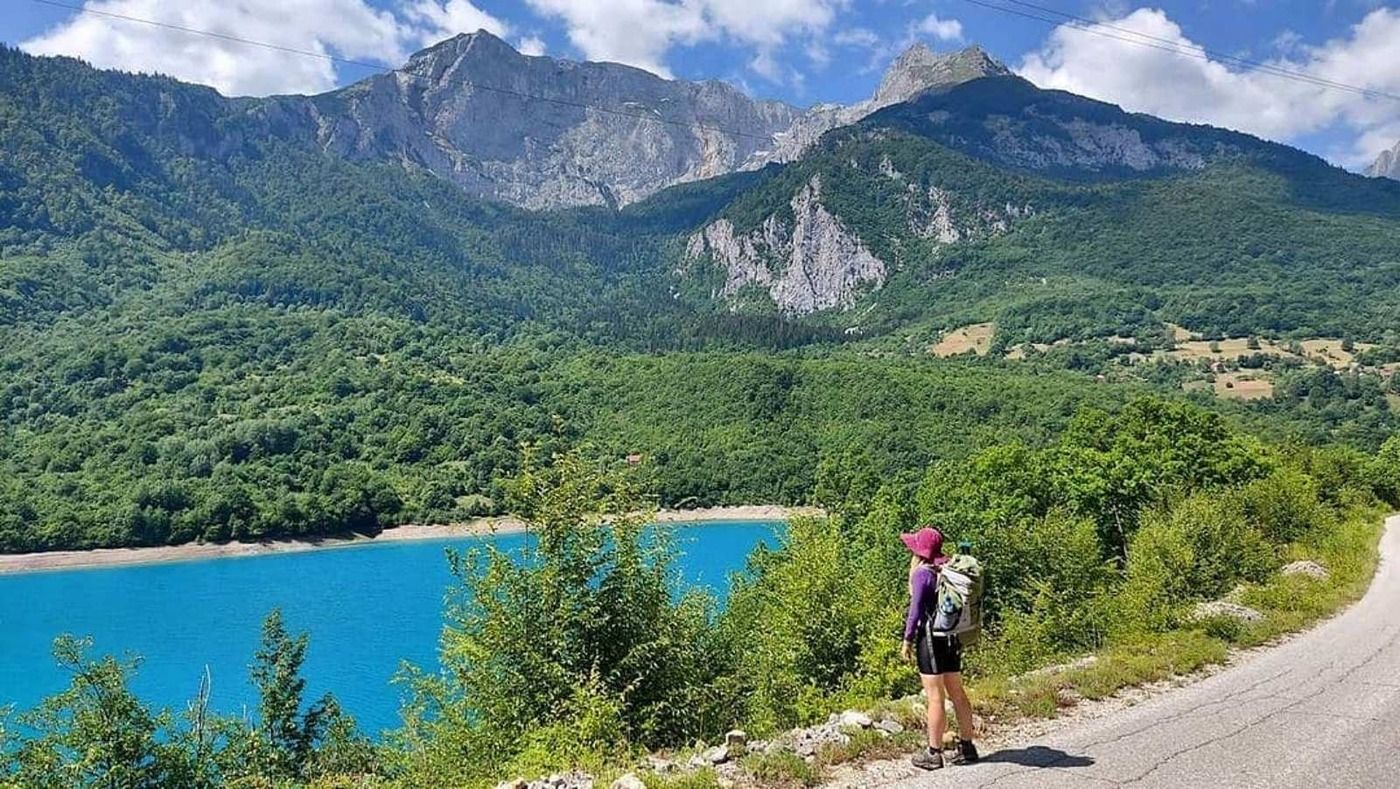 A hiker with a backpack looking out over the stunningly blue Piva Lake and the surrounding mountains.