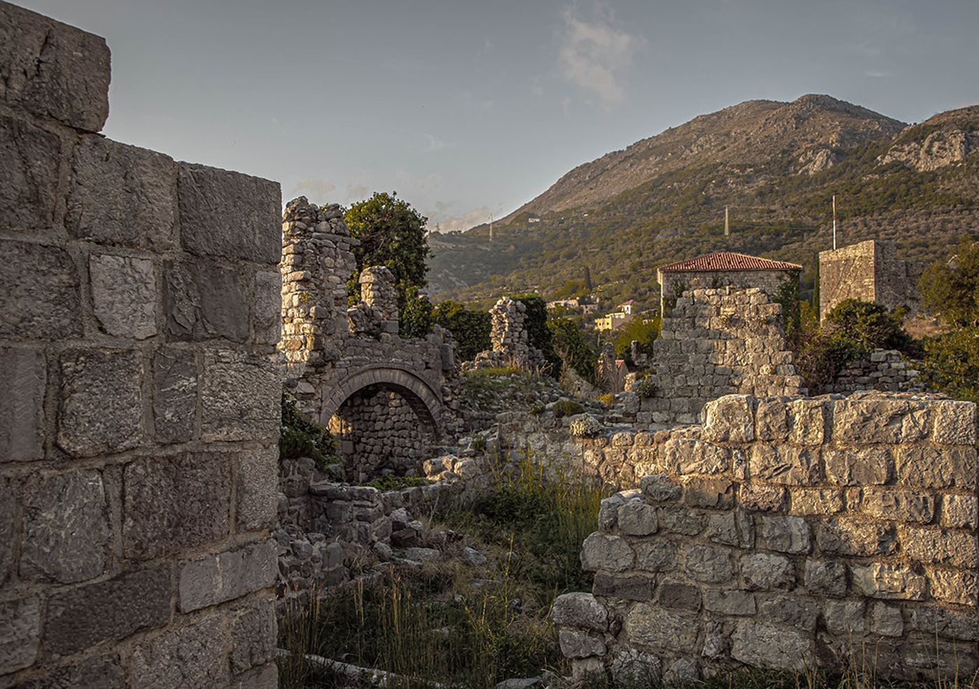 The atmospheric stone ruins of buildings and arches inside Stari Bar, with a mountain visible in the distance.