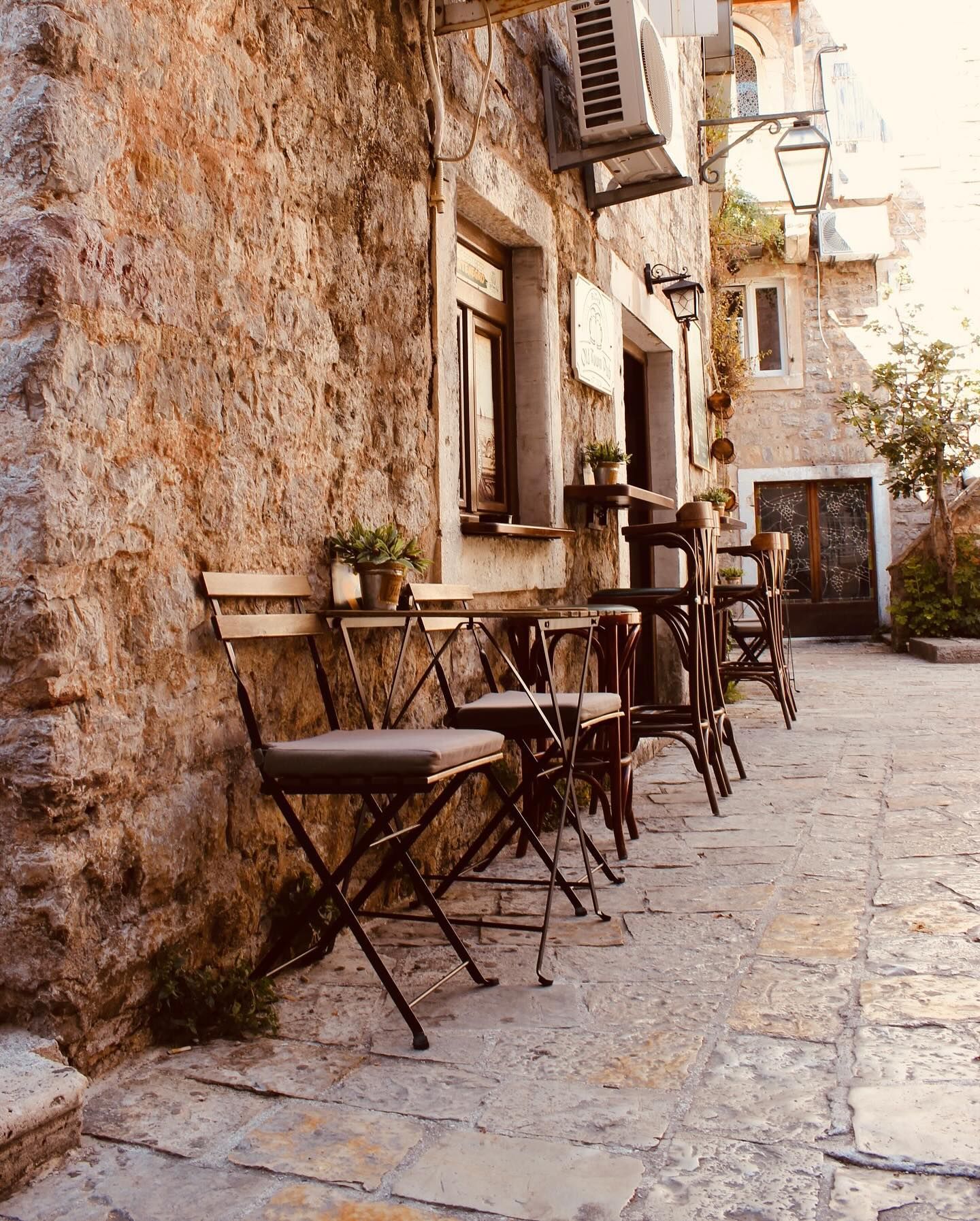 Outdoor seating of the pub on a historic stone-paved street, with simple wooden tables and chairs against an ancient stone wall.