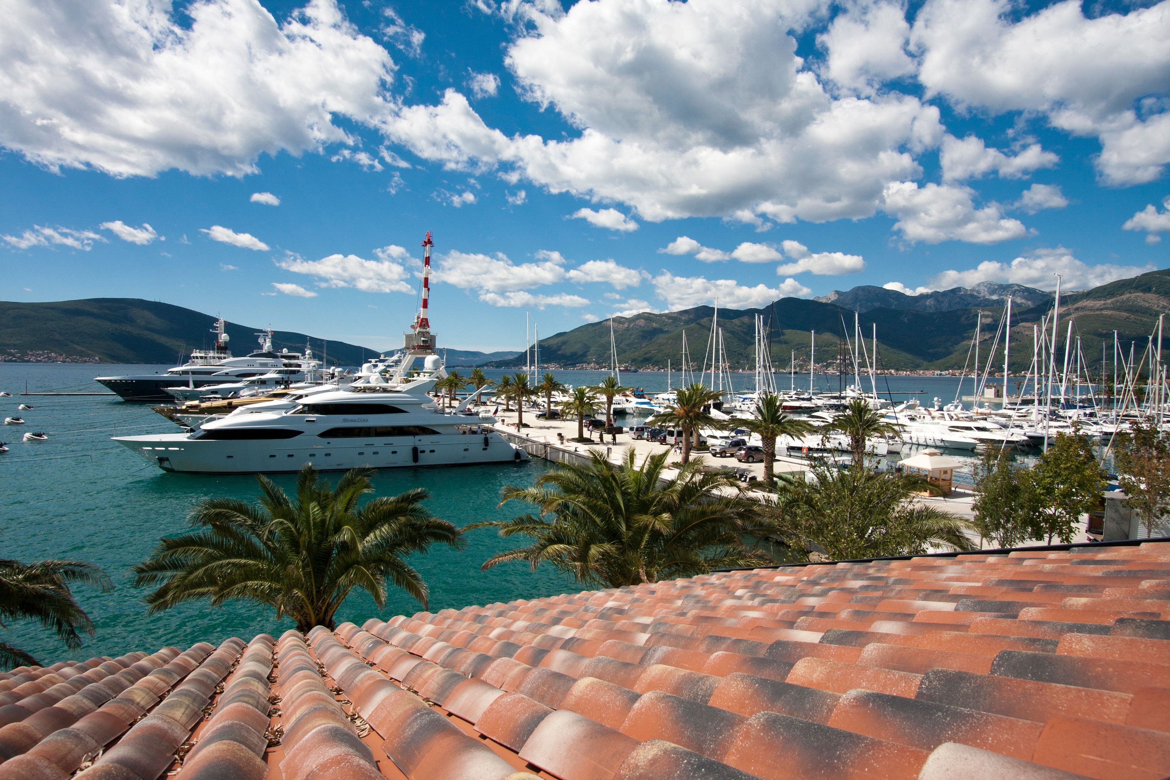 A high-angle view of the Porto Montenegro marina in Tivat, filled with luxury superyachts, with mountains in the background.