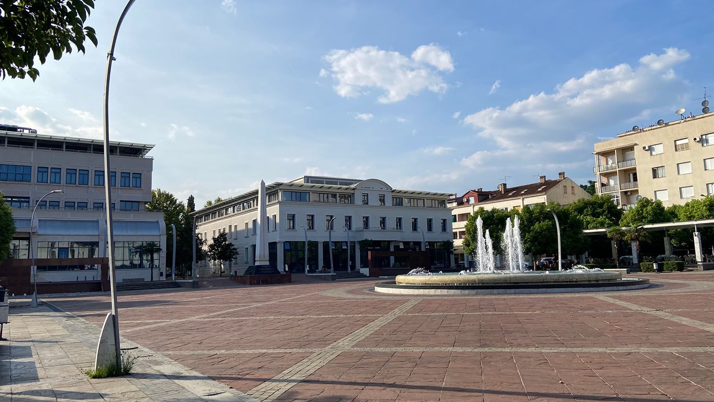 The fountain on Independence Square on a sunny day, with modern city buildings and trees in the background.