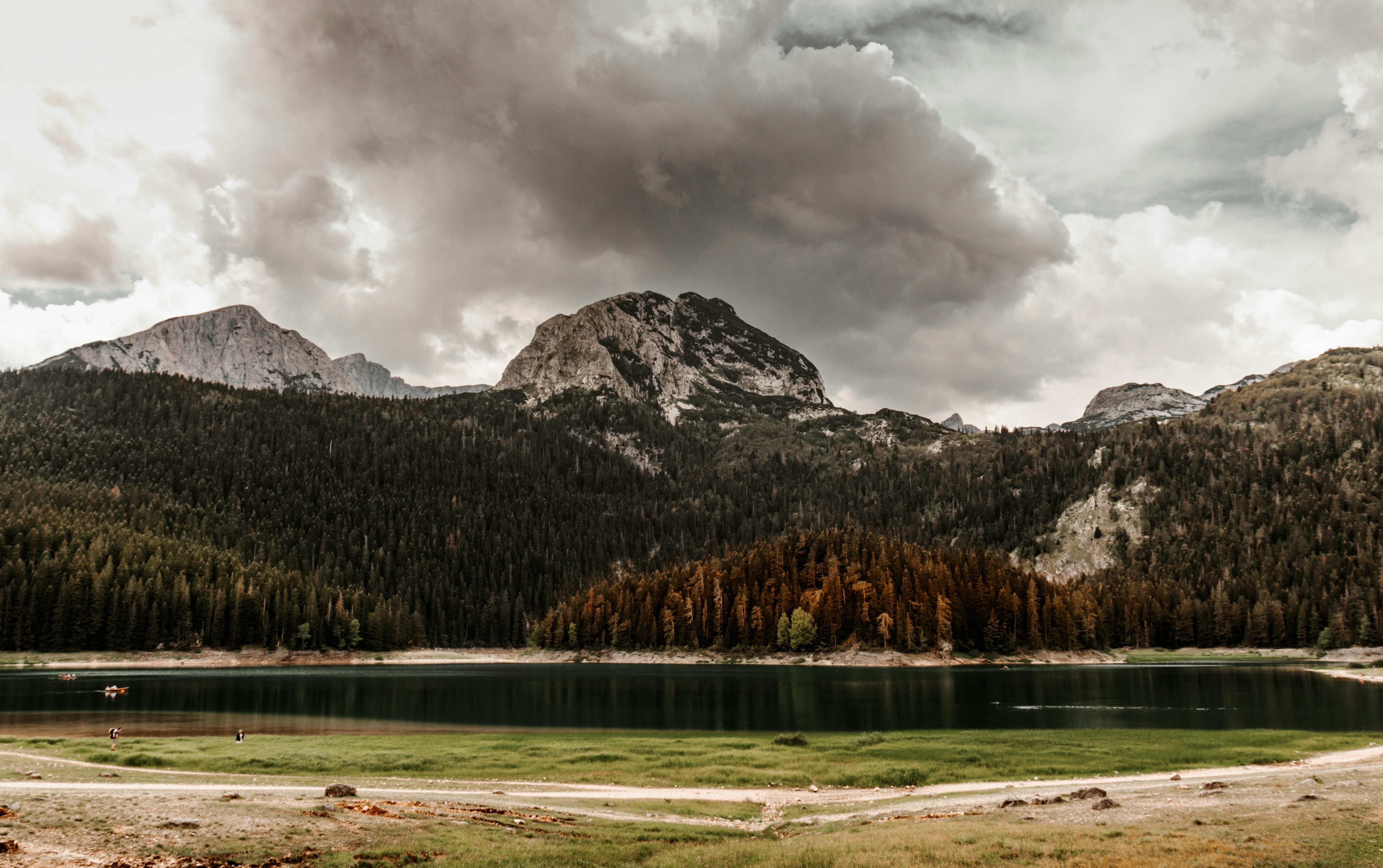 A dramatic view of Crno Jezero (Black Lake) and the surrounding mountains under heavy, atmospheric clouds.