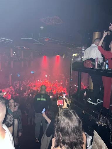 The crowded interior of Maximus nightclub, with a crowd dancing under red party lights, seen from an upper balcony.