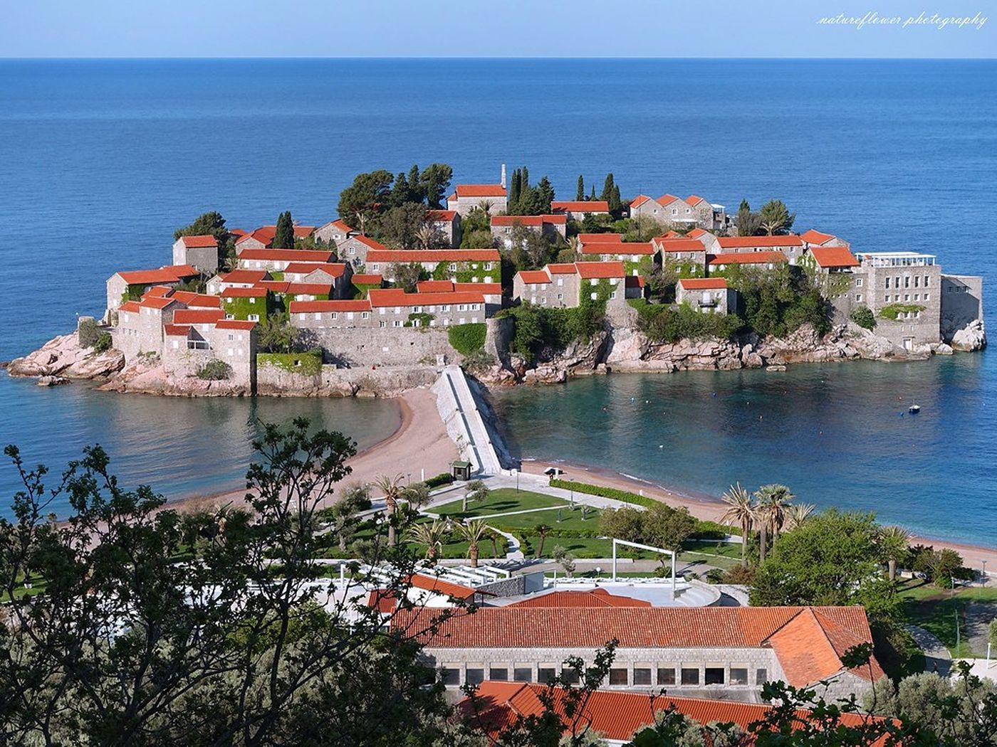 A classic viewpoint of the historic Sveti Stefan island hotel, showing the causeway and the blue Adriatic Sea.