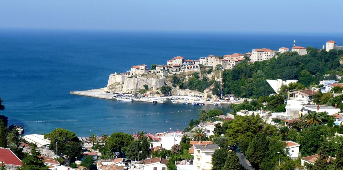 A panoramic view of the historic Old Town of Ulcinj, Montenegro, a fortified city on a rocky peninsula overlooking the Adriatic Sea and a small beach
