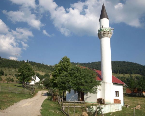 The small, white Dacići Mosque with its tall minaret, situated in the rural countryside of Rožaje, Montenegro, surrounded by green hills and forests