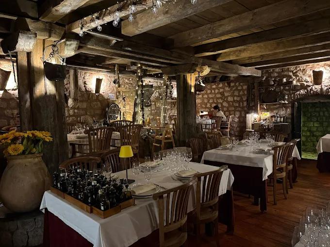The warm and rustic interior of Stari Mlini restaurant, featuring exposed stone walls, thick wooden ceiling beams, and elegantly arranged dining tables.