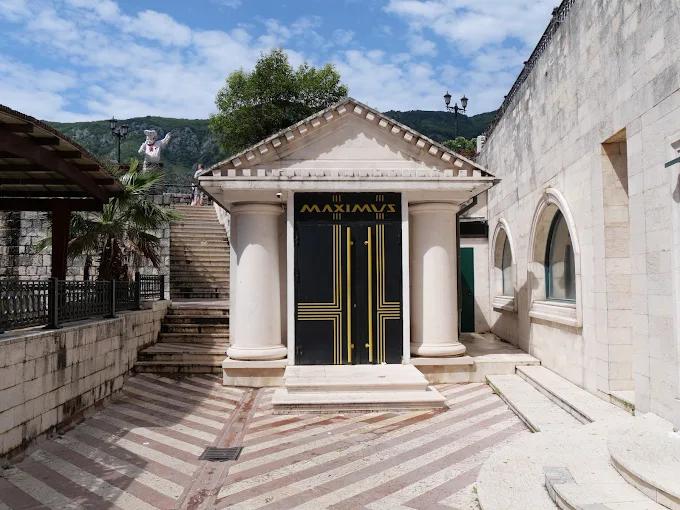 The classical-style entrance of Maximus nightclub in Kotor, with stone columns and an imposing black door.